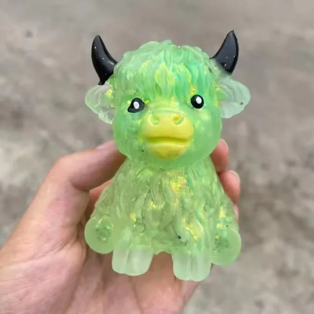 A hand holds a bright green glitter Highland cow squishy stress relief toy with black horns.