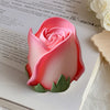 A pink rose silicone candle mold with green leaves resting on a white surface next to a piece of paper.