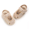Pair of beige soft sole sandals for baby's first steps featuring cute bear appliqués