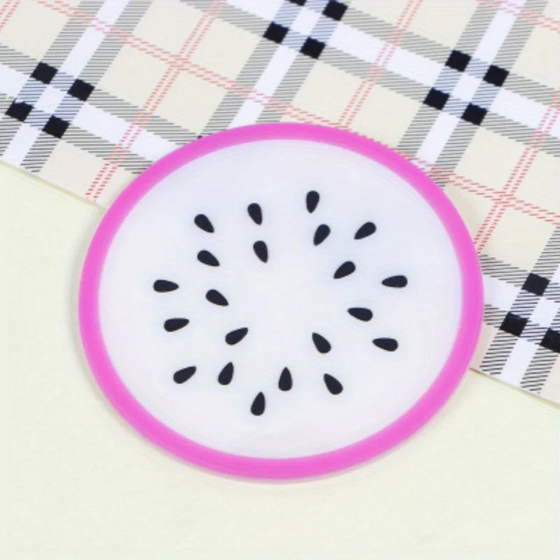 A round pink silicone coaster with a black fruit pattern rests on a plaid fabric surface.