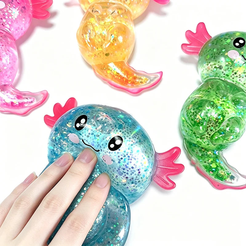A hand is holding a blue glitter axolotl squishy stress relief toy next to other colorful axolotl toys.