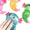 A hand is holding a blue glitter axolotl squishy stress relief toy next to other colorful axolotl toys.
