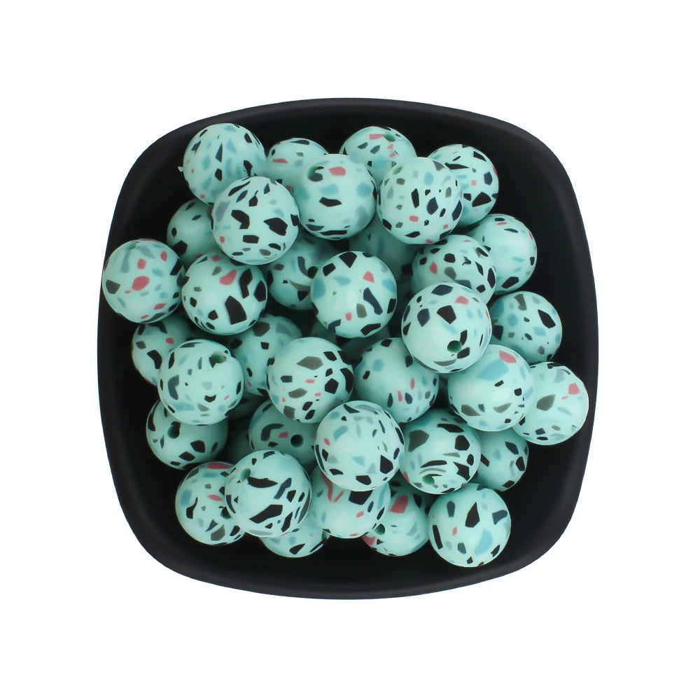 A black bowl filled with small, round, printed silicone beads in leopard and daisy patterns.