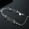 A delicate sterling silver snake chain bracelet with small spherical beads and a charm displayed on a dark surface.