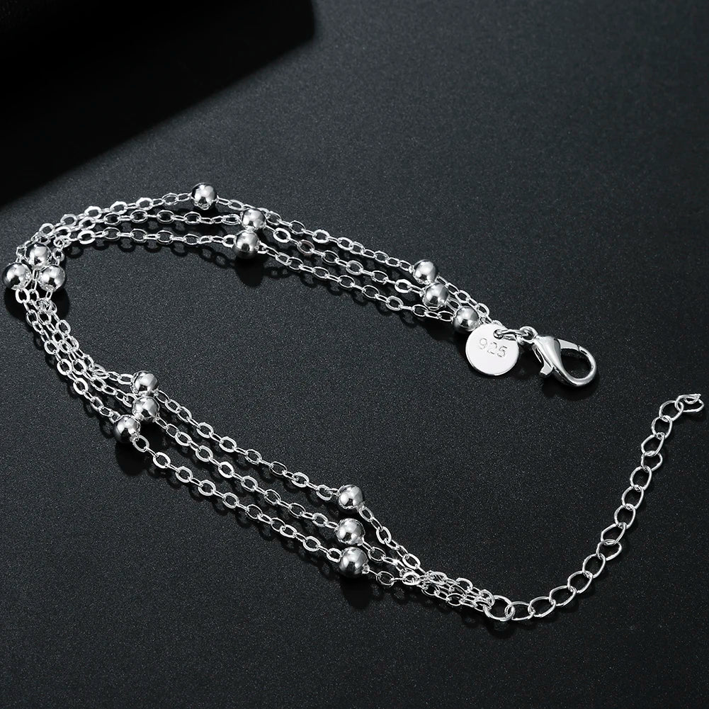 A delicate sterling silver snake chain bracelet with small spherical beads and a charm displayed on a dark surface.