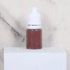 A small glass bottle of reddish-brown paint sits on a white surface.