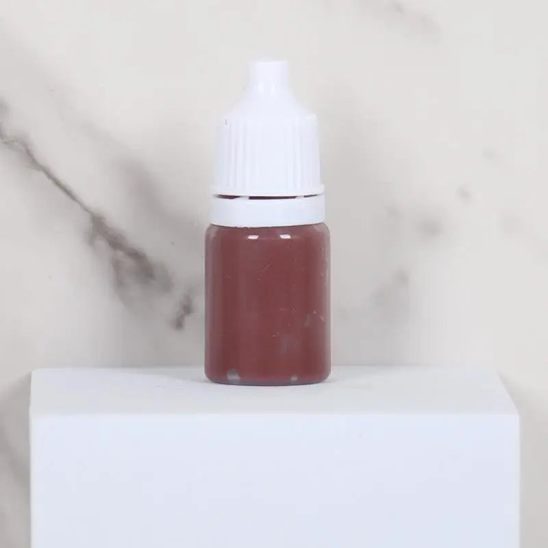 A small glass bottle of reddish-brown paint sits on a white surface.