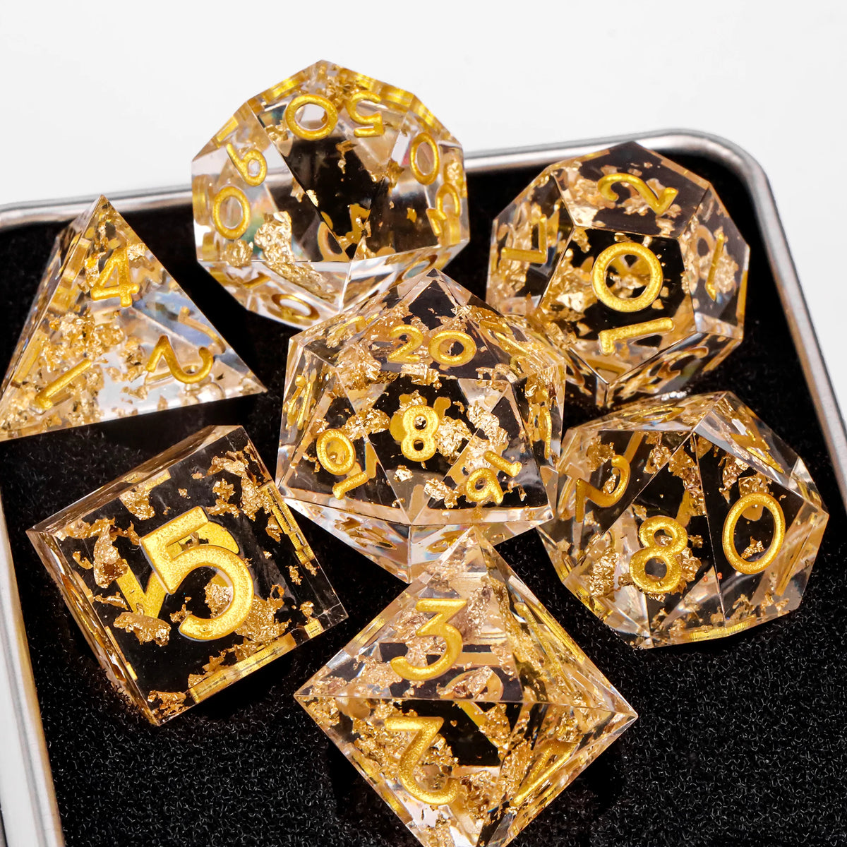 A set of ten handmade resin sharp edge dice in gold and black are displayed on a dark surface.