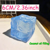 A translucent blue ice cube shaped squishy stress ball for coconut oil filling resting on a white surface.