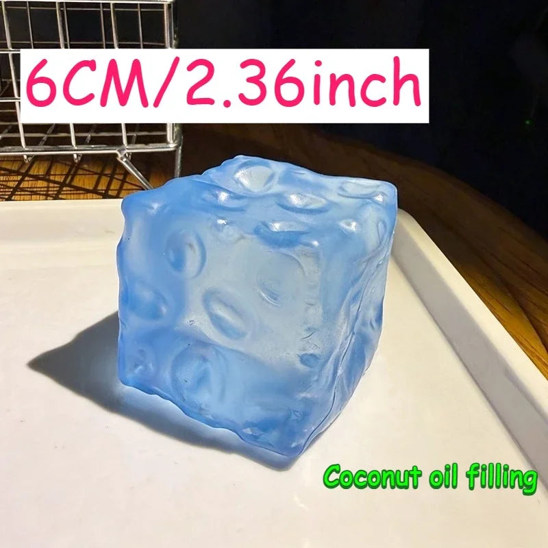 A translucent blue ice cube shaped squishy stress ball for coconut oil filling resting on a white surface.