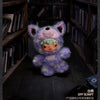 A purple and green plush doll pendant featuring an animal face in a dimly lit bookshelf setting.
