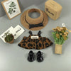 A leopard print sling dress for plush dolls displayed with a straw hat, woven box, and shoes.