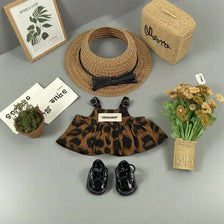 A leopard print sling dress for plush dolls displayed with a straw hat, woven box, and shoes.