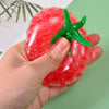 A hand holds a bright red squishy tomato stress relief fidget toy with green stem and leaves.