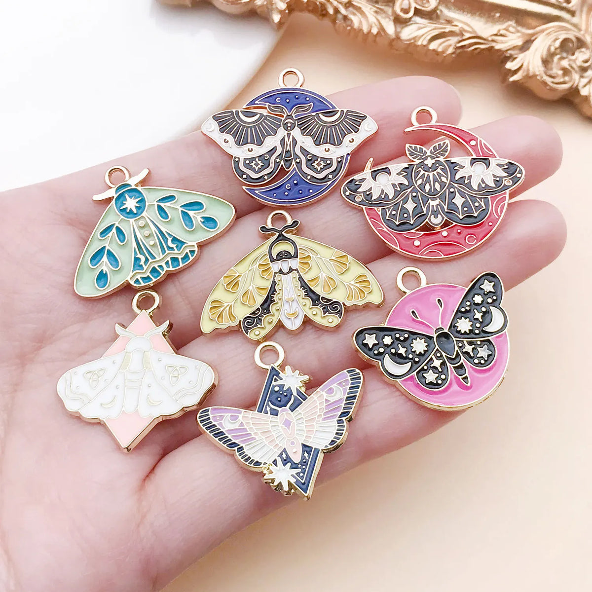 A hand holds several colorful butterfly drop charms for jewelry making