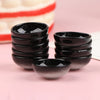 A stack of ten glossy black miniature dollhouse rice bowls on a pink surface.