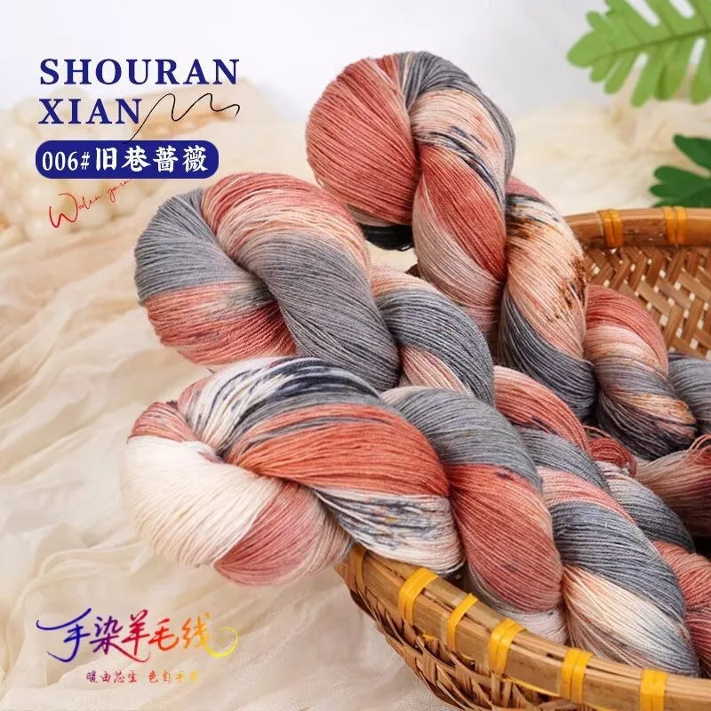 A bundle of hand-dyed yarn in a gradient of pink, gray, and white wool, coiled and resting in a woven basket.