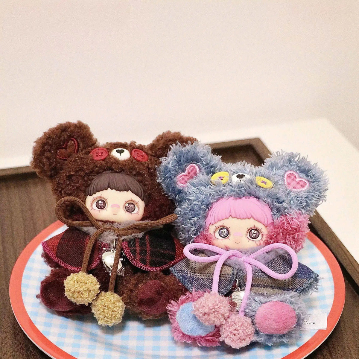 A plush charm of a bear character with brown fur and pink accents displayed on a round plate.