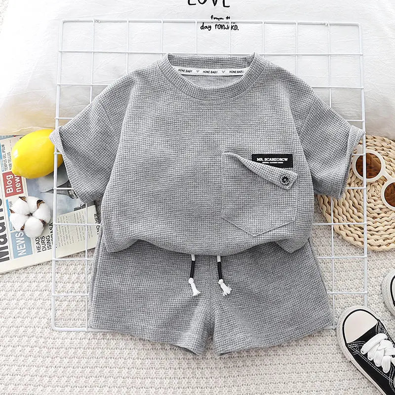 A gray boys' summer cotton t-shirt and shorts set laid out on a white grid background.
