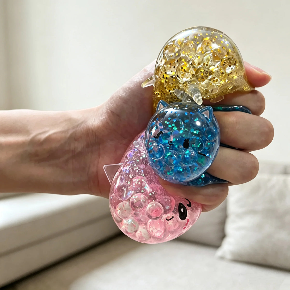 A hand holds a clear squishy stress ball shaped like a purple unicorn with iridescent glitter inside.