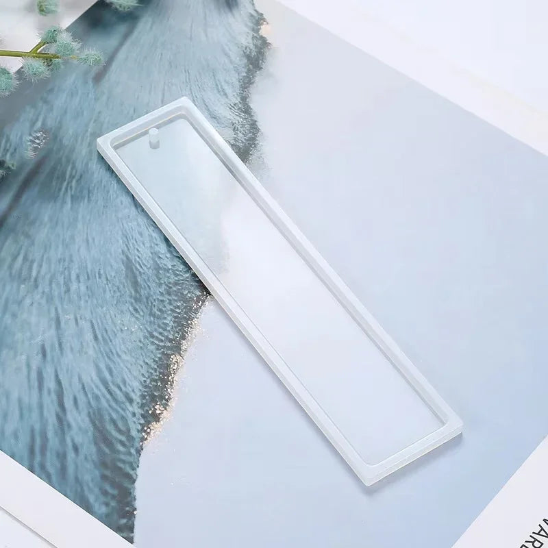 A clear flexible silicone mold for resin bookmarks is shown next to a textured blue background.