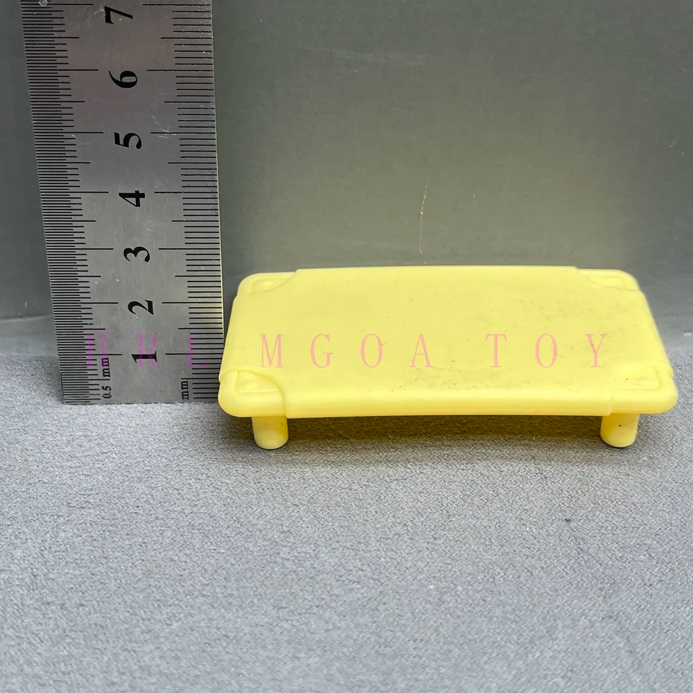 Yellow rectangular plastic toy with molded letters MGOATOY placed next to a ruler.