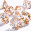 A collection of polyhedral dice with a clear, galaxy finish and gold accents are displayed on a white surface.