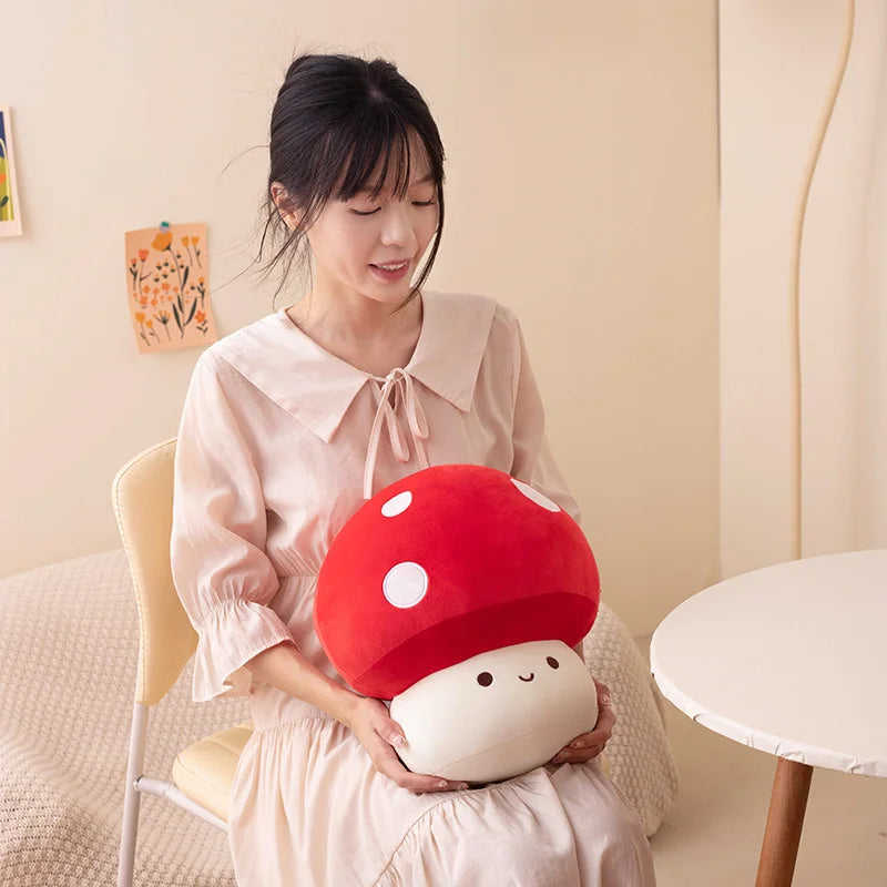 A woman holds a red and white mushroom plush pillow in a light pink dress.