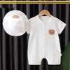 A white cotton muslin baby romper and hat set with a brown bear appliqué hanging on a wooden hanger.