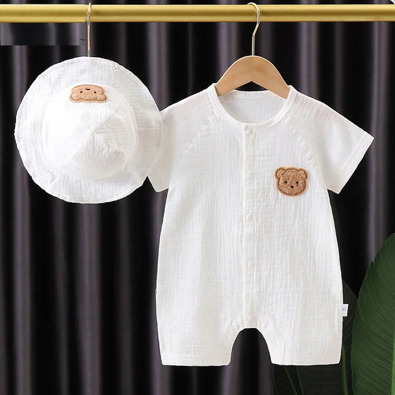 A white cotton muslin baby romper and hat set with a brown bear appliqué hanging on a wooden hanger.