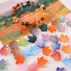 A string of amber and brown glass beads shaped like maple leaves is displayed on a piece of paper.