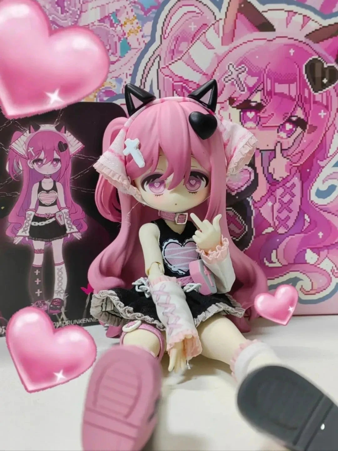 A pink anime-style vinyl art figure with black cat ears and pink hair is displayed in a box featuring pink and purple designs