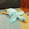 A light blue plush goose pillow with orange beak and feet lying on a light blue surface.