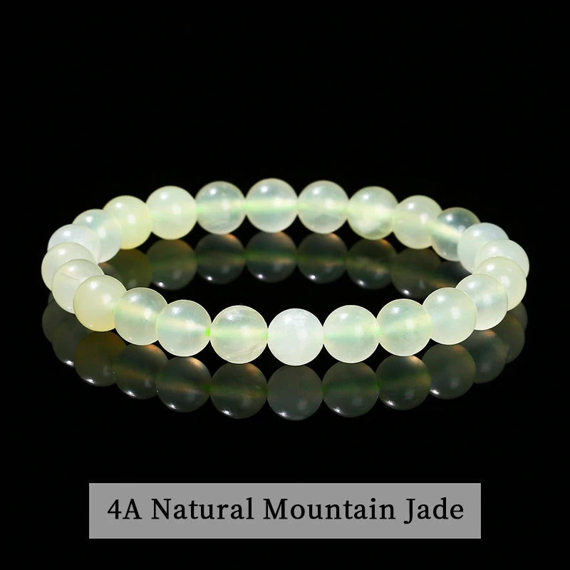 A bracelet of light green natural mountain jade beads displayed on a reflective surface.