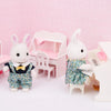 A white rabbit doll dressed in a green floral outfit sits next to a pink miniature furniture set.