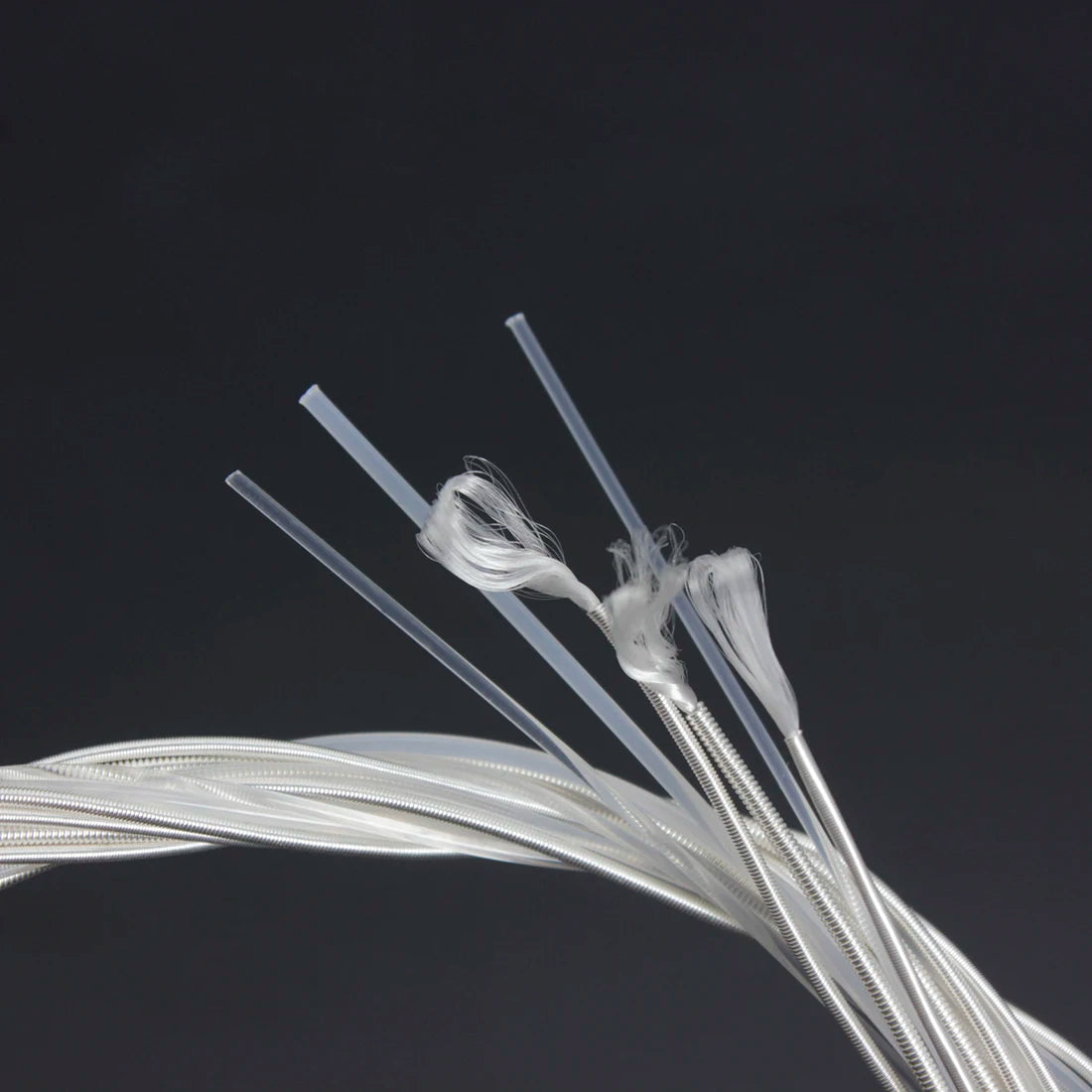 A close-up view of silver-plated classical guitar strings with transparent nylon cores against a dark background.