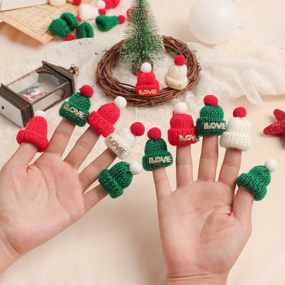 A hand displays various mini knitted hats and scarves in red, green, and white for Christmas doll dress-up accessories.