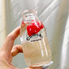 A hand holds a clear glass bottle filled with liquid and red fruit pieces, used as a drink cup toy.