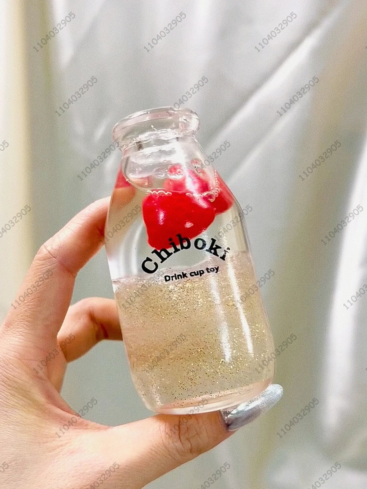 A hand holds a clear glass bottle filled with liquid and red fruit pieces, used as a drink cup toy.