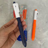 A hand holds a white and blue retractable water spray pen next to an orange pen and its packaging.