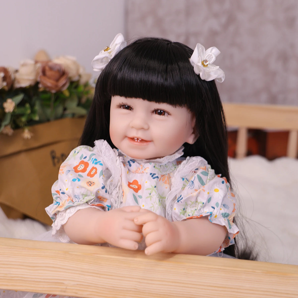 A lifelike reborn baby doll with soft cloth body has long black hair and white flowers in her hair.