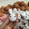 A hand holds a white crocheted rabbit keychain among various brown and gray animal figures.