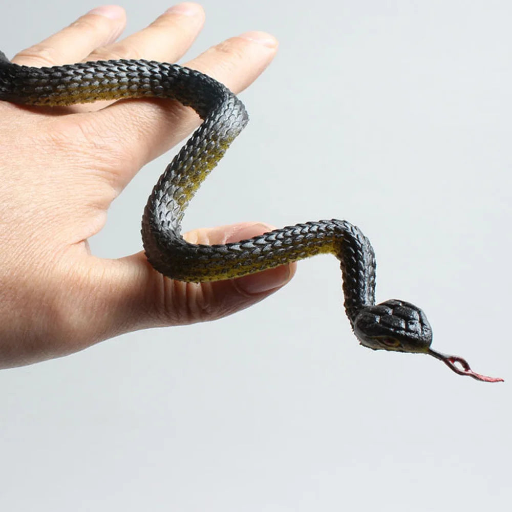 A hand is holding a realistic rubber snake prop with dark green and black patterned skin.
