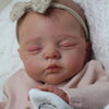 A lifelike 19-inch reborn baby doll with a soft cloth body wearing a headband and pink clothing.