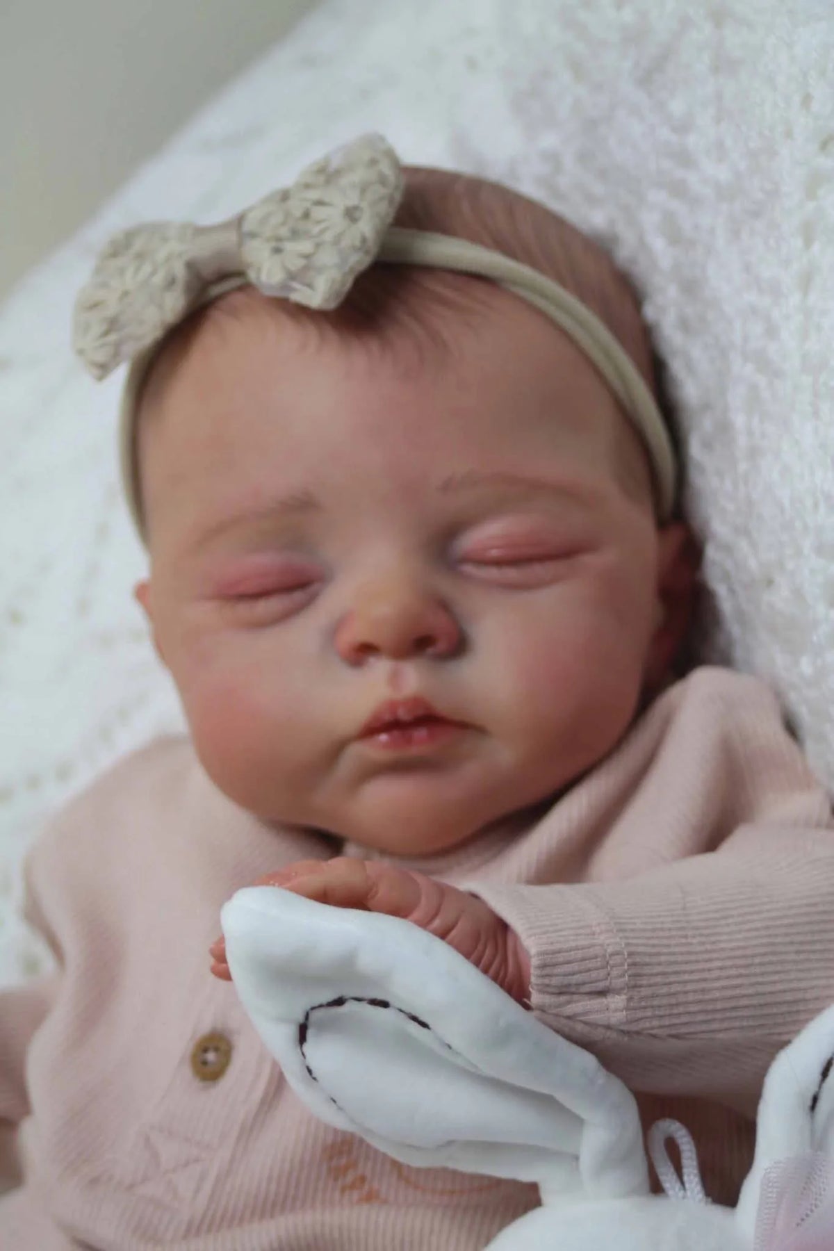 A lifelike 19-inch reborn baby doll with a soft cloth body wearing a headband and pink clothing.