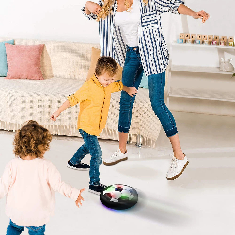 A woman is holding a floating soccer ball with LED lights and music while a child plays nearby.