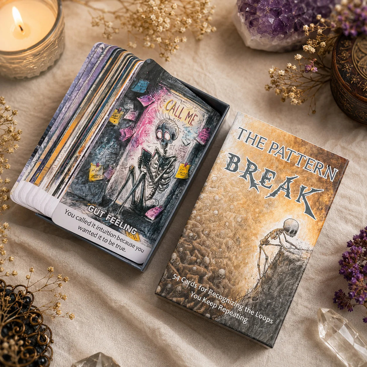A deck of Pattern Break oracle cards lying on a beige fabric next to dried flowers and crystals.