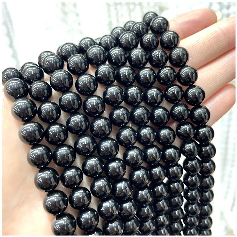 A hand holds a string of small, dark, polished natural stone beads for DIY jewelry making.