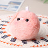 A pink fluffy plush pig keychain resting on a patterned fabric surface.