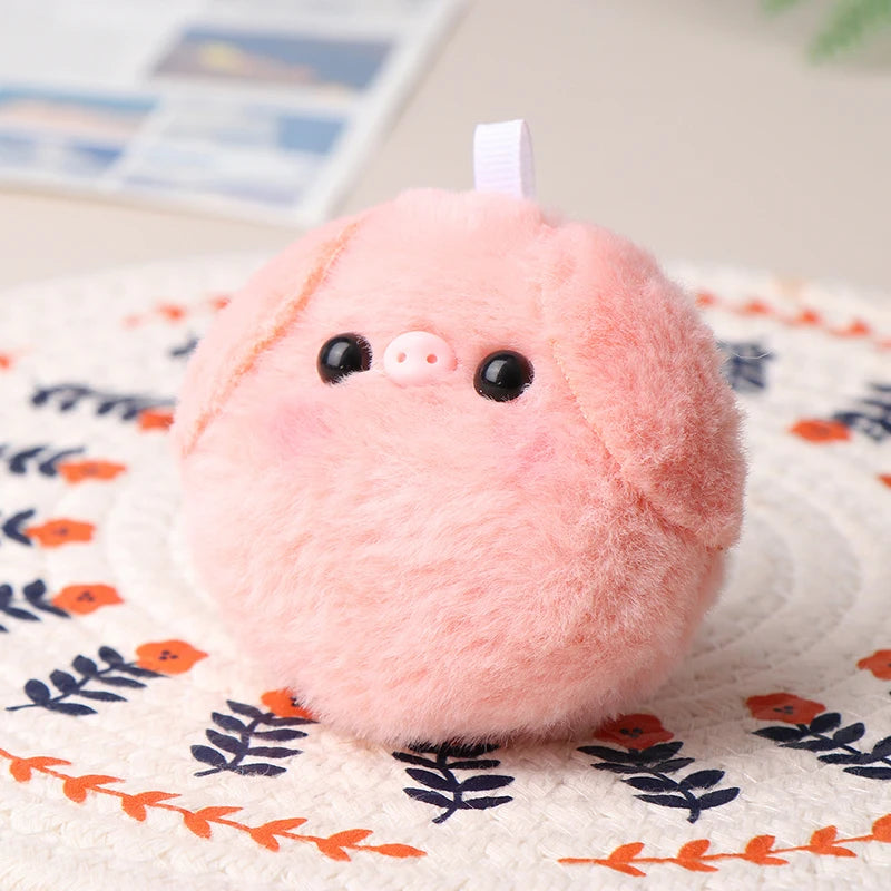 A pink fluffy plush pig keychain resting on a patterned fabric surface.